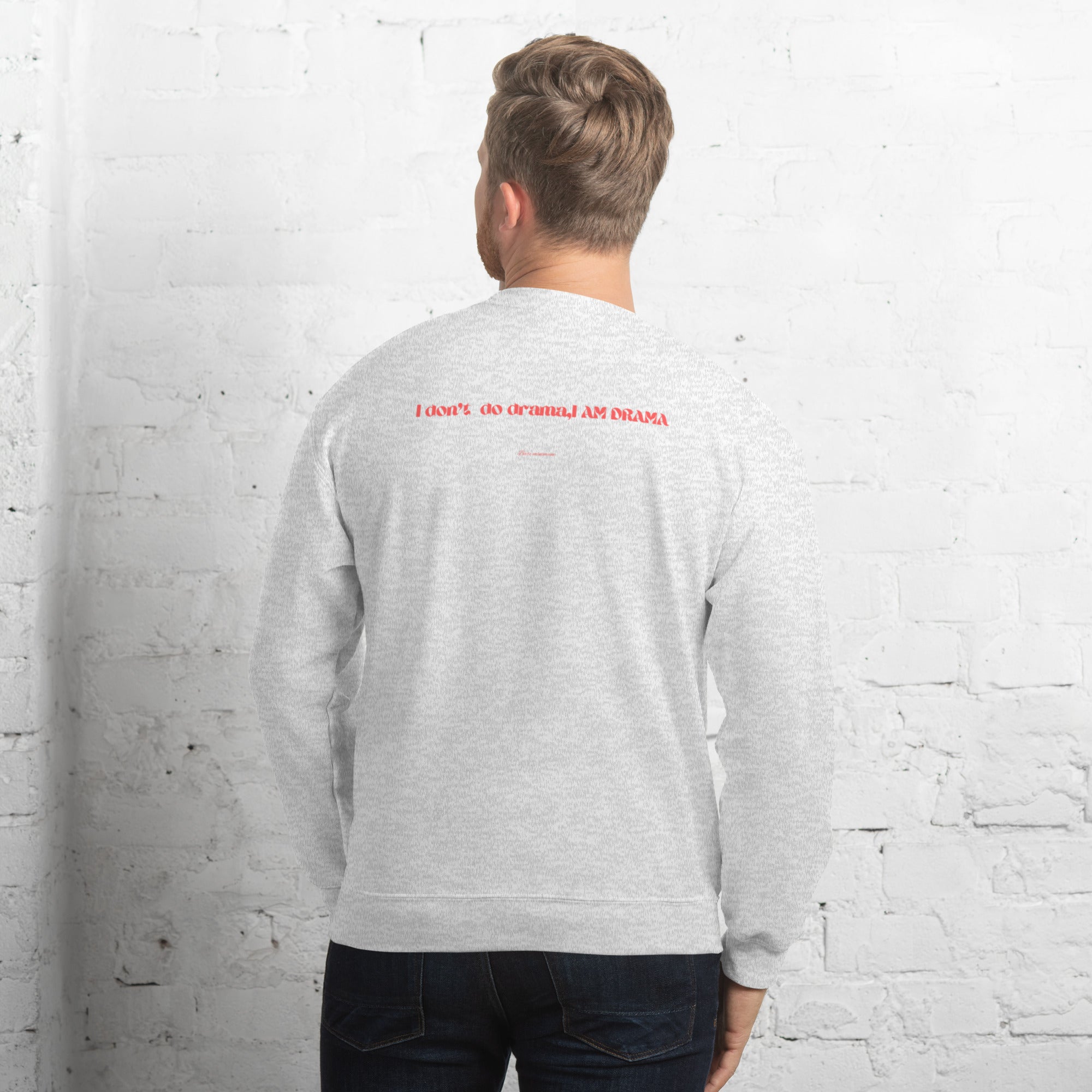 Person wearing a gray sweatshirt with red text on the back against a white brick wall.